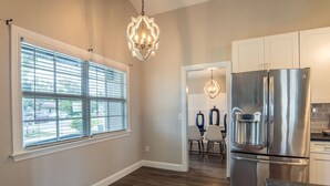 A modern kitchen with a stainless steel refrigerator, a chandelier, and a dining area with chairs and a table.