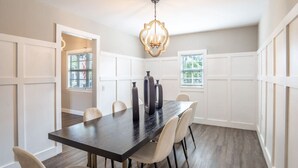 A dining area with a dark wooden table, white chairs, and a chandelier.