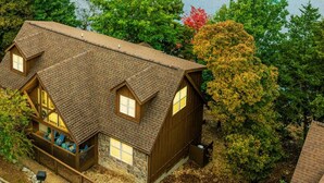 Ein Holzhaus mit geneigtem Dach, umgeben von Bäumen und einem Gewässer.