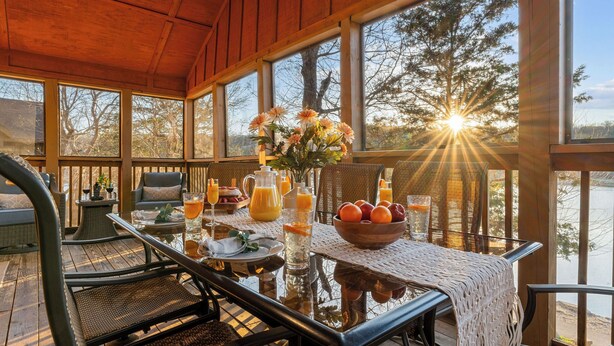 Eine Holzterrasse mit einem Frühstückstisch, mit Blick auf ein Gewässer und Bäume.