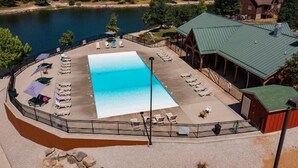 Ein großer Pool mit Liegestühlen und Sonnenschirmen, umgeben von einer Holzterrasse und einem Gebäude mit Gründach.