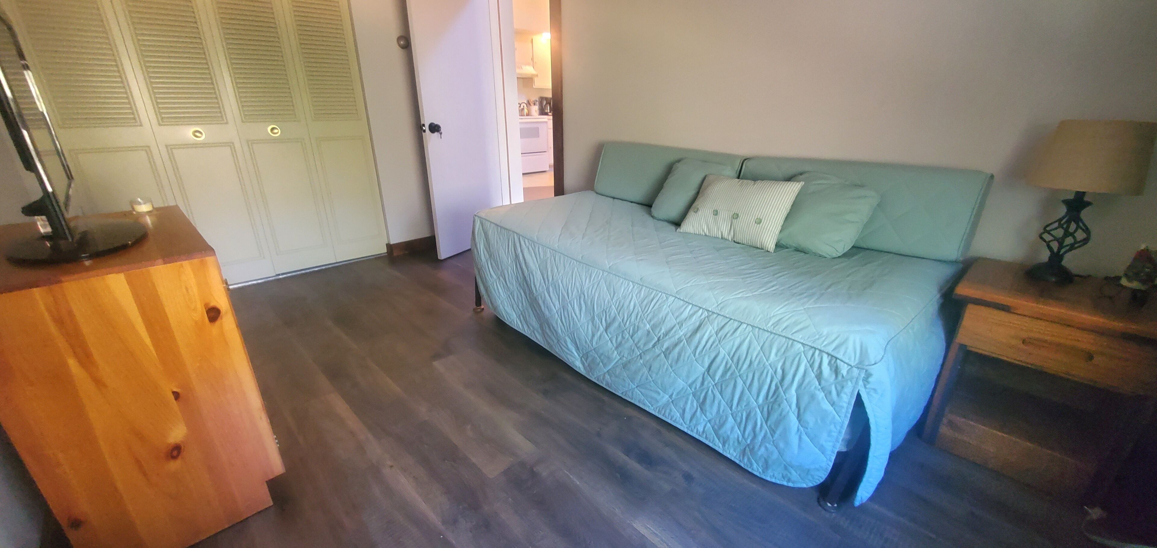 A bedroom with a bed, wooden dresser, and a nightstand with a lamp.