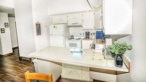 A compact kitchen with white cabinets, a stove, and a sink. There is a wooden chair and a small plant on the counter. - Gateway Condo Unit 25 - 12 to 15 minute drive to Killington Mountain (Mendon)
