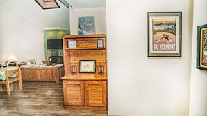 A cozy living room with a wooden cabinet, a sofa, and a framed picture of a skier. - Gateway Condo Unit 25 - 12 to 15 minute drive to Killington Mountain (Mendon)