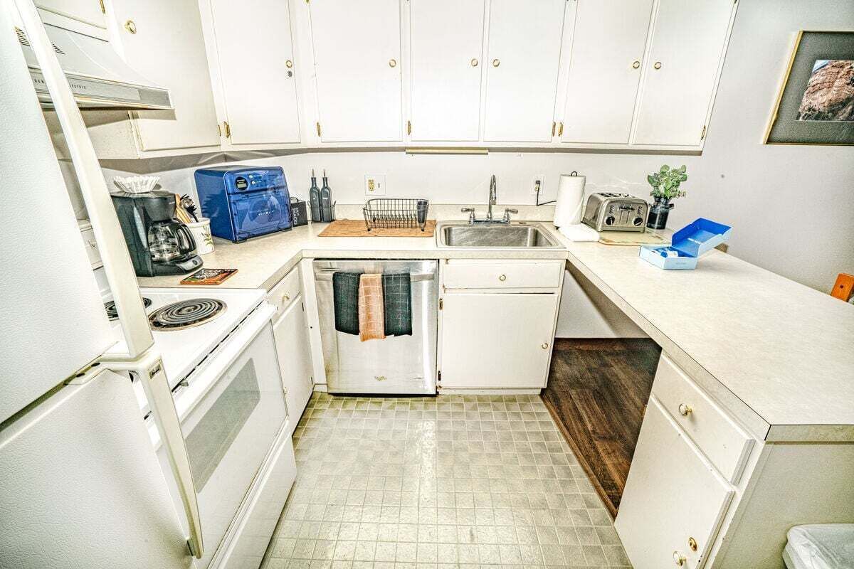 Una cocina compacta con gabinetes blancos, estufa, pileta y una pequeña zona de encimera.