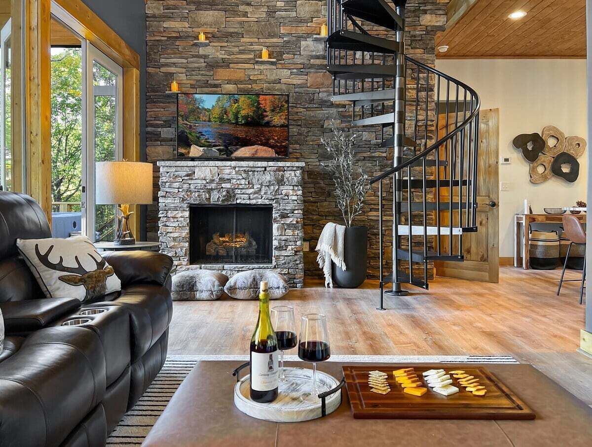 A modern living room with a stone fireplace, leather sofa, and a wine bottle on a tray.