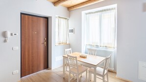 A room with a wooden door, a white table with four chairs, a window with sheer curtains, and a white radiator. - La Posteria Junior Suite 1 by icasamia.it (Orino)