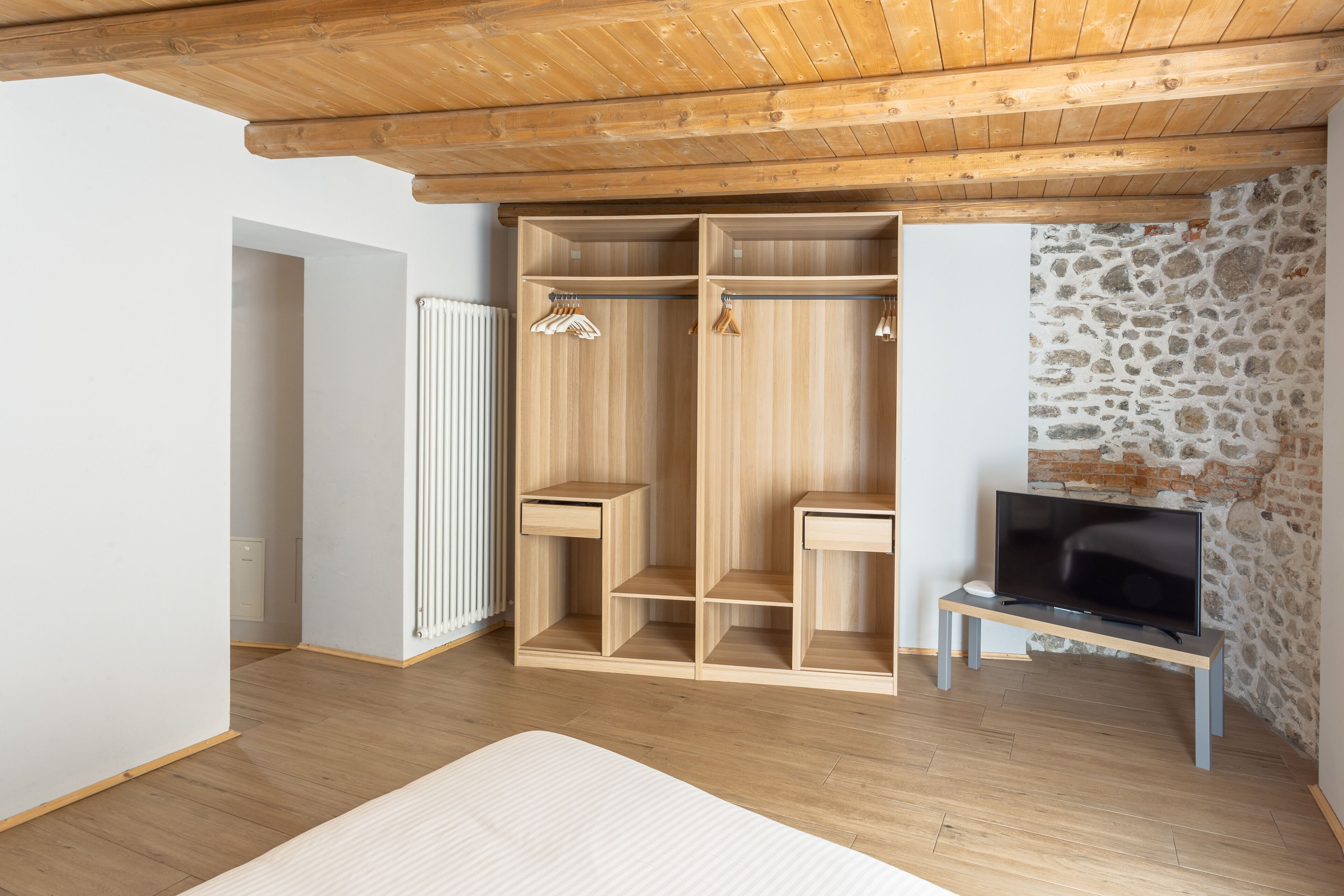 A room with a wooden wardrobe, a television on a stand, and a stone wall.