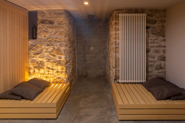 A spa room with stone walls, a wooden bench, and a shower area.