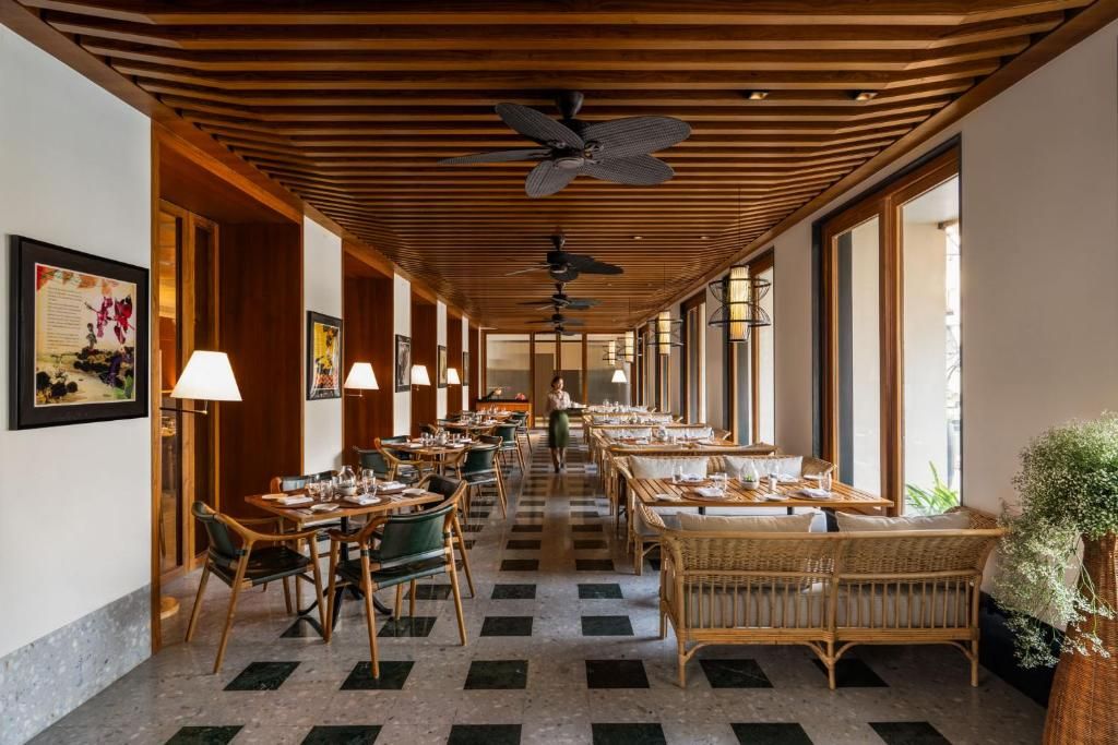 A hotel corridor with dining tables, chairs, ceiling fans, and large windows.