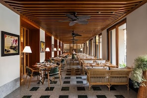 Ein Hotelgang mit Esstischen, Stühlen, Deckenventilatoren und großen Fenstern.