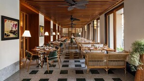 Un pasillo de hotel con mesas de comedor, sillas, ventiladores de techo y ventanas amplias.