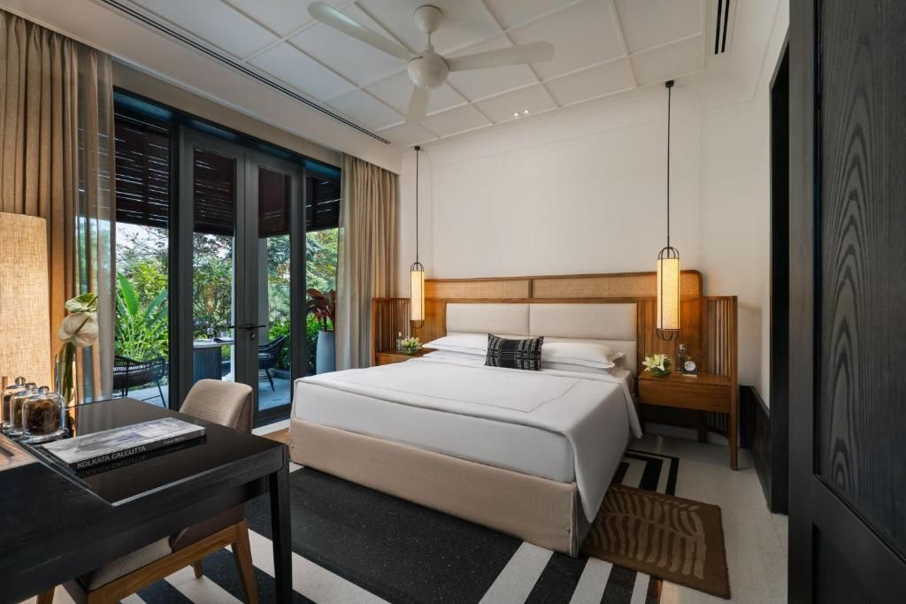 A hotel room with a bed, bedside tables, a desk, and a view of greenery outside.