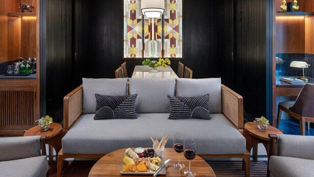 A modern living room with a sofa, two side tables, a chandelier, and a dining area with a table and chairs. - Taj Taal Kutir Kolkata (Burdwan)