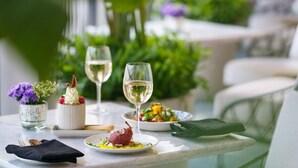 A dining table with plates of food, glasses of white wine, and a small vase with flowers. - Taj Taal Kutir Kolkata (Burdwan)