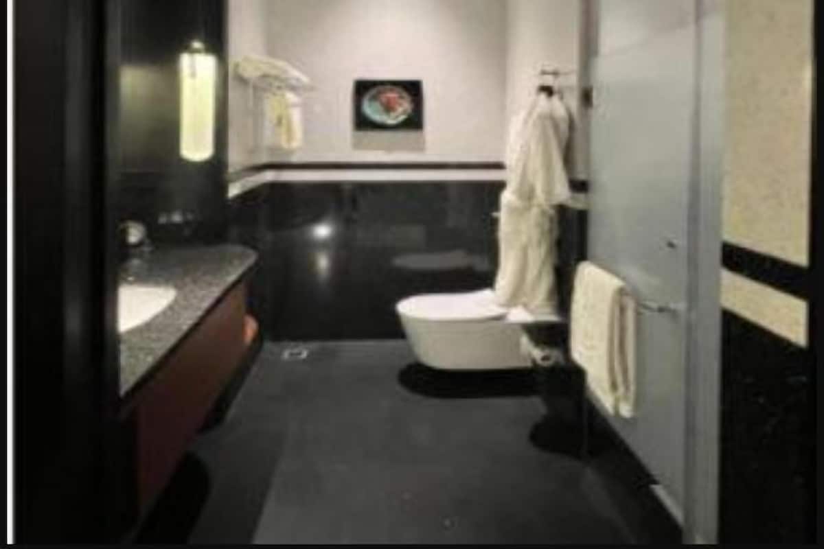 Une salle de bain moderne avec un carrelage foncé, des toilettes blanches, un lavabo avec un miroir et un porte-serviettes.