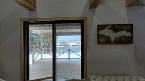 Een kamer met een schuifglasdeur die leidt naar een terras met uitzicht op het strand en de oceaan. Er staat een comfortabele bank en een kaart van Upper Peninsula, Michigan hangt aan de muur.