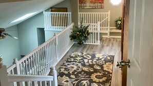 A multi-level interior with a wooden staircase, a patterned rug, and a door with a round light fixture above it. - NEW Beautiful, Spacious Lake House  (Angola)