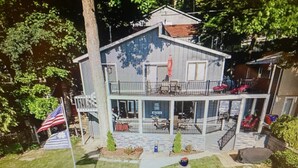 A two-story house with a covered patio and a flagpole with an American flag. - NEW Beautiful, Spacious Lake House  (Angola)