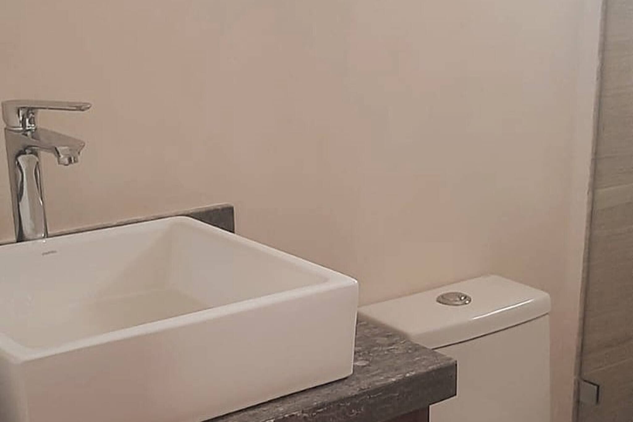 A bathroom with a white sink, a toilet, and a marble countertop.