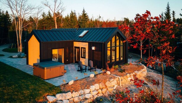 Une maison moderne dotée d’une grande terrasse, d’un mur en pierre et donnant sur une forêt.