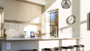 Une cuisine moderne dotée d’un îlot central, de tabourets de bar, de luminaires suspendus et d’une horloge au mur.