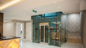 A modern lobby with a glass elevator, marble flooring, and a reception desk.