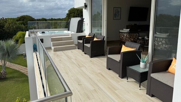 A modern outdoor living area with a hot tub, wicker furniture, and a glass door leading to an indoor space. - Cove Bay Villa II "THE PENTHOUSE"  (Anguilla)