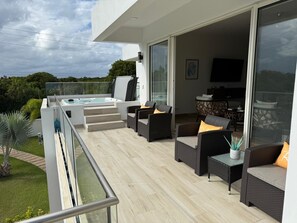 Een modern buitenverblijf met een jacuzzi, rieten meubels en een glazen deur die leidt naar een binnenruimte.