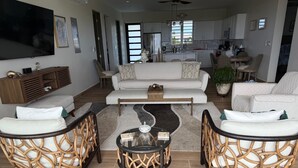 A modern living room with a sofa set, two wicker chairs, a coffee table, and a TV mounted on the wall. - Cove Bay Villa II "THE PENTHOUSE"  (Anguilla)
