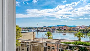 Une vue depuis un balcon donnant sur une marina, avec des bateaux, une étendue d’eau et des bâtiments en arrière-plan.