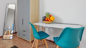 Une pièce avec une table blanche, des chaises turquoise, un miroir, une armoire et un panier de fruits.