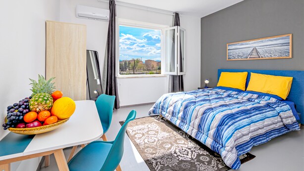 Une chambre moderne avec un lit, une table à manger avec des chaises, un panier de fruits et une fenêtre avec des rideaux.