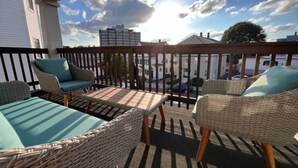 Un espacio al aire libre techado con mobiliario de mimbre y cojines, con vistas a un cuerpo de agua y edificios.