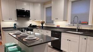 Una cocina moderna con armarios blancos, un microondas negro y una isla grande con taburetes.