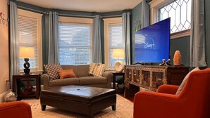 Una sala de estar con un sofá, una mesa de centro y dos sillones. Hay un televisor sobre un mueble bajo, y una chimenea con repisa.