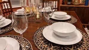 Una mesa de comedor dispuesta con platos, cuencos y copas de vino, rodeada de individuales estampados.