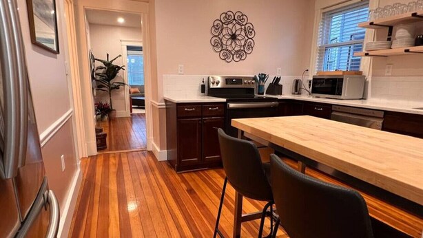 Una cocina moderna con suelo de madera, una isla central con taburetes de bar, electrodomésticos de acero inoxidable y un elemento decorativo en la pared.
