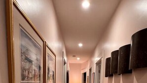 Un pasillo con cuadros en las paredes, suelo de madera y una lámpara a lo lejos.