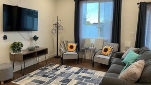 A living room with a flat-screen TV, two armchairs with sunflowers, a sofa, a patterned rug, and a floor lamp. - Cozy, Modern home in Lindon. (North)