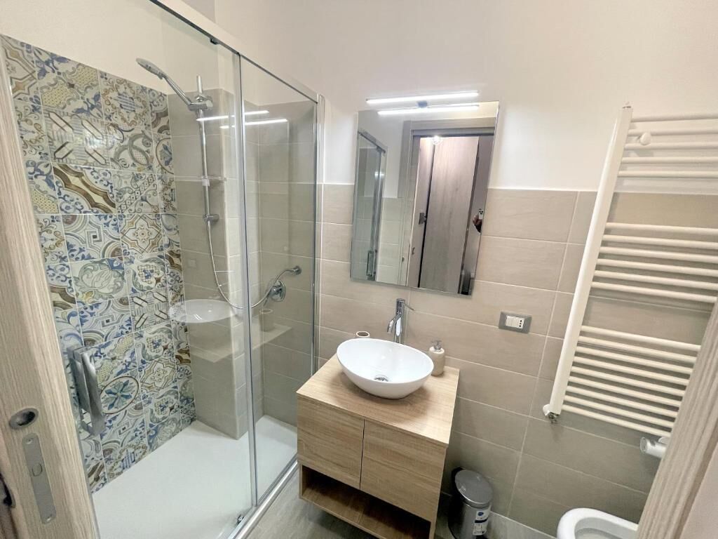 A modern bathroom with a glass shower enclosure, a wooden vanity with a white sink, and a tiled backsplash.