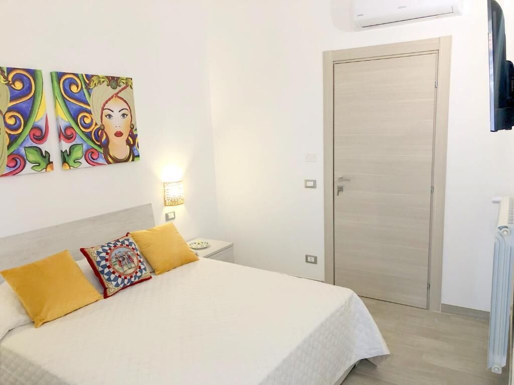 A bedroom with a bed, a nightstand, a wall-mounted air conditioner, and a door.