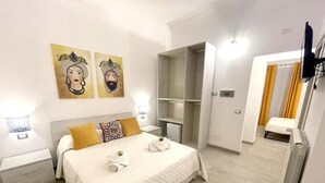 Quarto de hotel com cama, guarda-roupa, mesa de cabeceira e televisão.