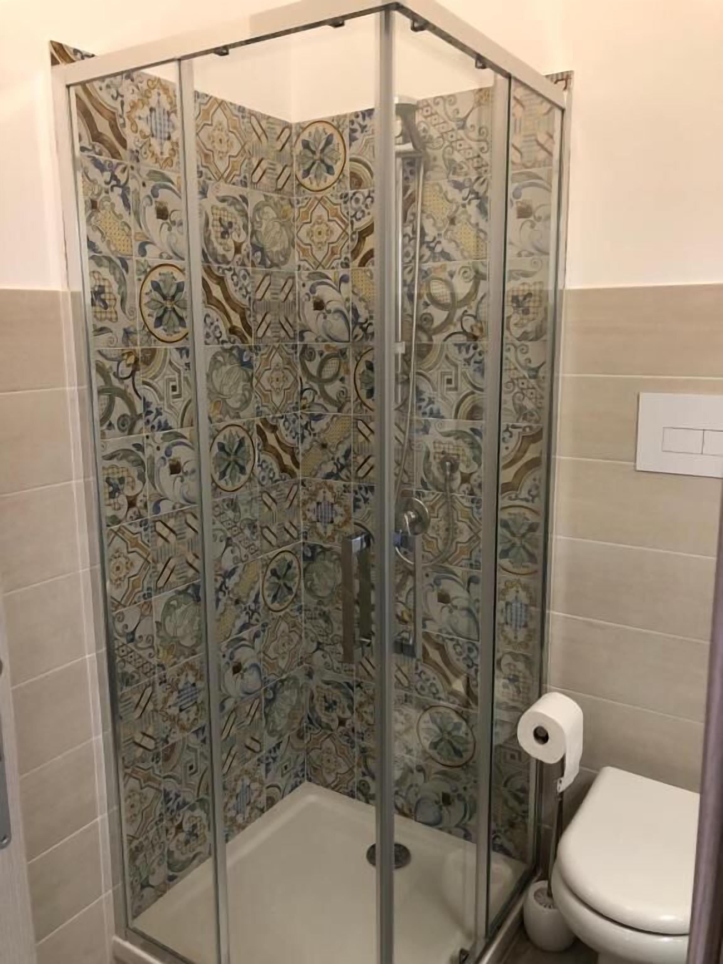Eine Dusche mit Glastür und Wand mit gemusterten Fliesen.