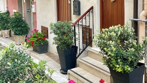 Um edifício com porta de madeira, varanda com grade e plantas em vasos à frente.