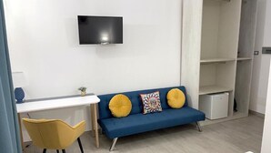 Uma sala de estar moderna com um sofá azul, almofadas amarelas, uma televisão de tela plana, uma mesinha e uma cadeira amarela.
