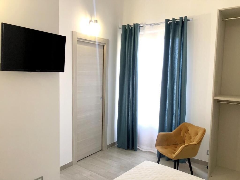 Un dormitorio con cama, televisor montado en la pared, armario y una silla.