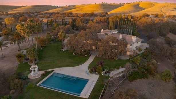 Uma casa grande com piscina, cercada por um gramado bem cuidado e árvores.