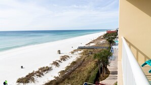 Blick auf den Strand vom Balkon aus, mit blauem Himmel, Sandstrand und ein paar Spaziergängern.