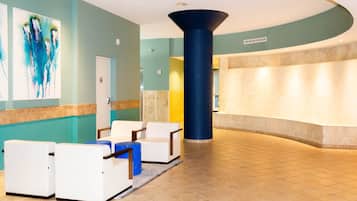 A lobby with a reception desk, white armchairs, a large blue pillar, and abstract art on the wall.